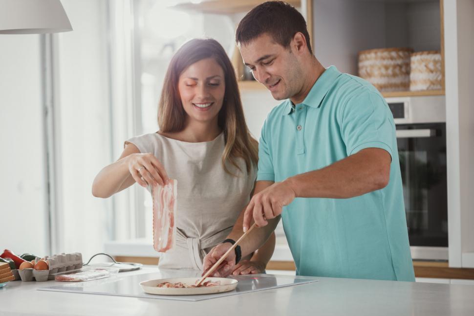 Free Image of Couple cooking bacon in a kitchen 