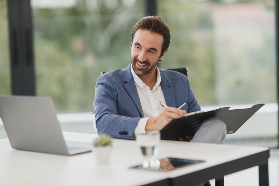 Free Image of Smiling businessman working on a clipboard 