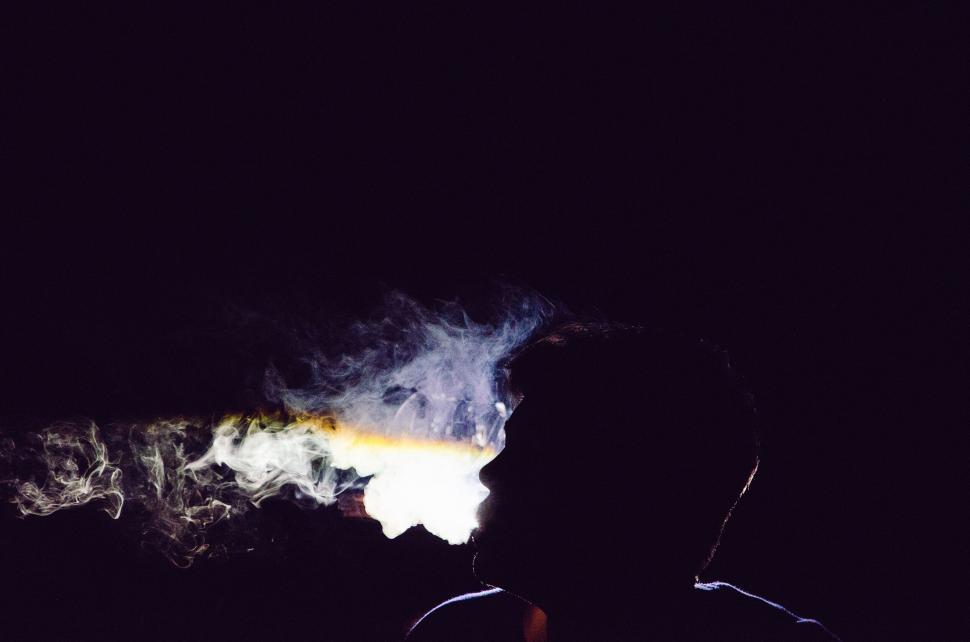 Free Image of Silhouette of a person blowing smoke against dark background 