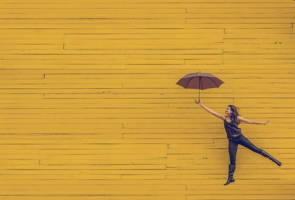 Free Image of Woman levitating with umbrella on yellow wall 