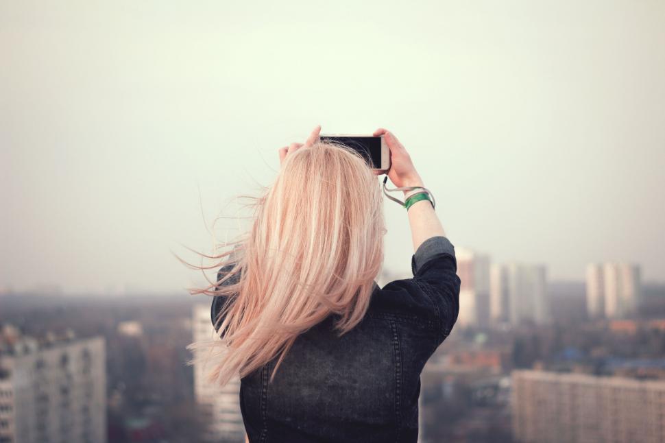 Free Image of Blonde woman taking a photo with her phone 