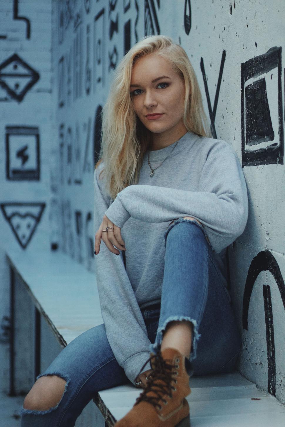 Free Image of Casual woman sitting in front of urban graffiti 