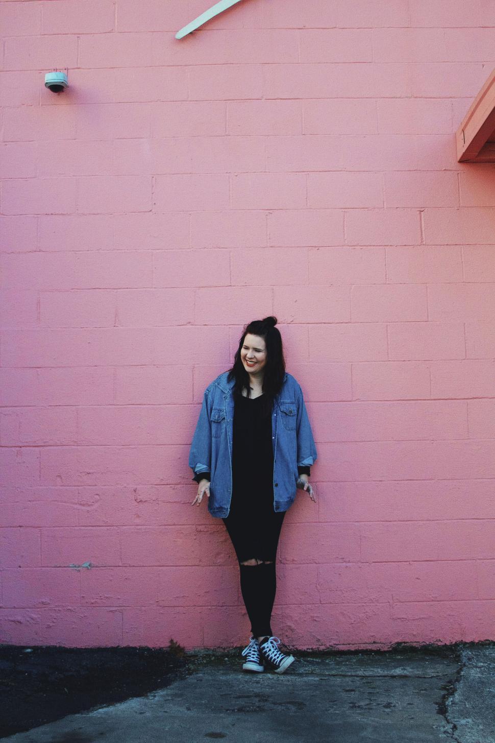 Free Image of Woman leaning against a pink wall with smile 