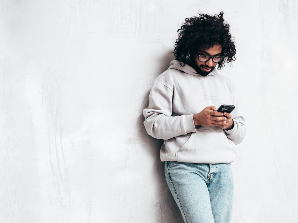 Free Image of A man leaning against a wall looking at a phone 