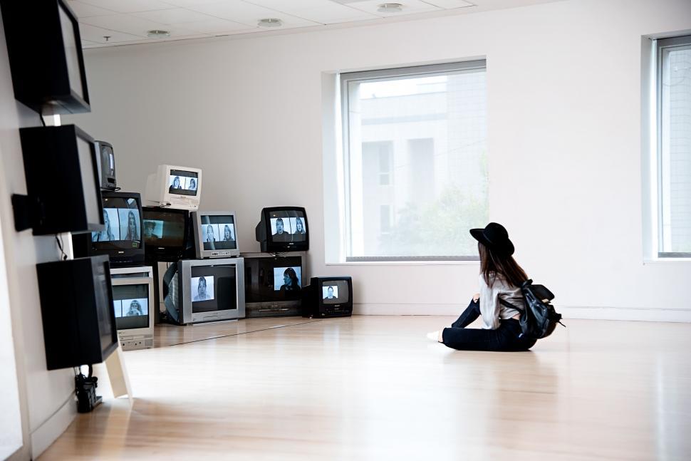 Free Image of Woman watching multiple televisions in a gallery 
