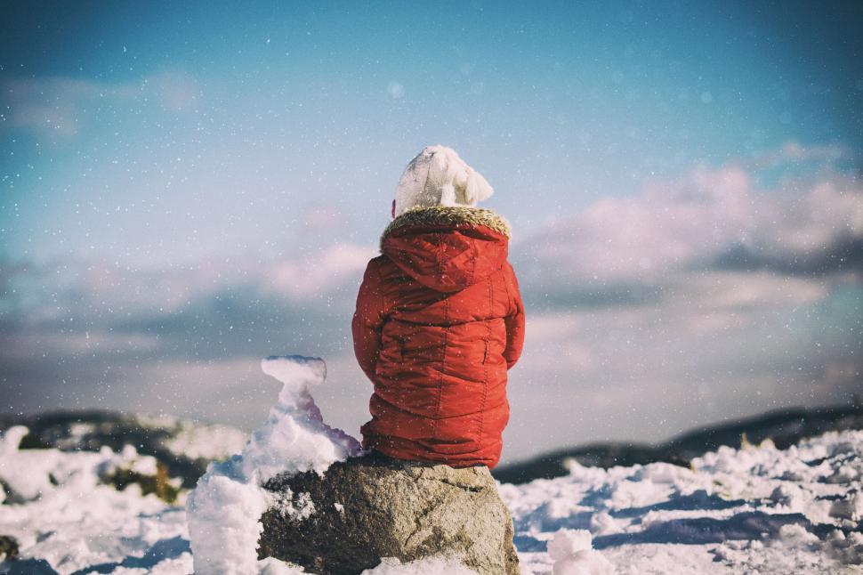 Free Image of Child in red jacket sitting on snowy rock 