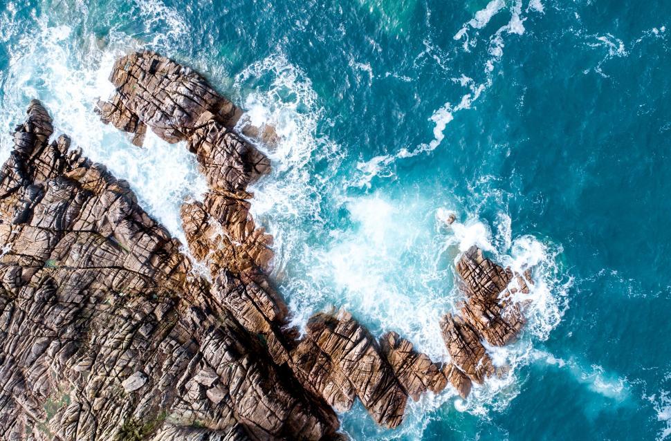 Free Image of Waves crashing on jagged rocks from above 