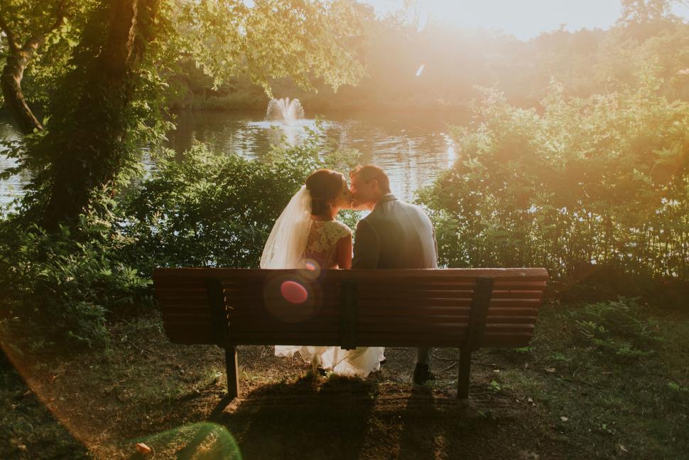 Free Image of Newlywed couple kissing on a park bench 