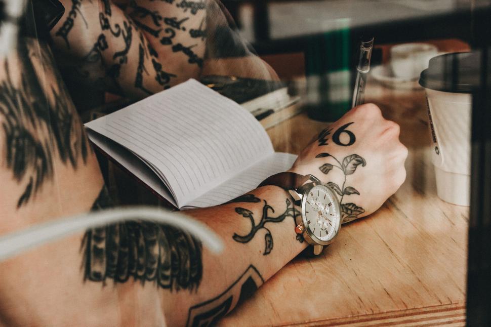 Free Image of Person writing in notebook with tattooed arms 