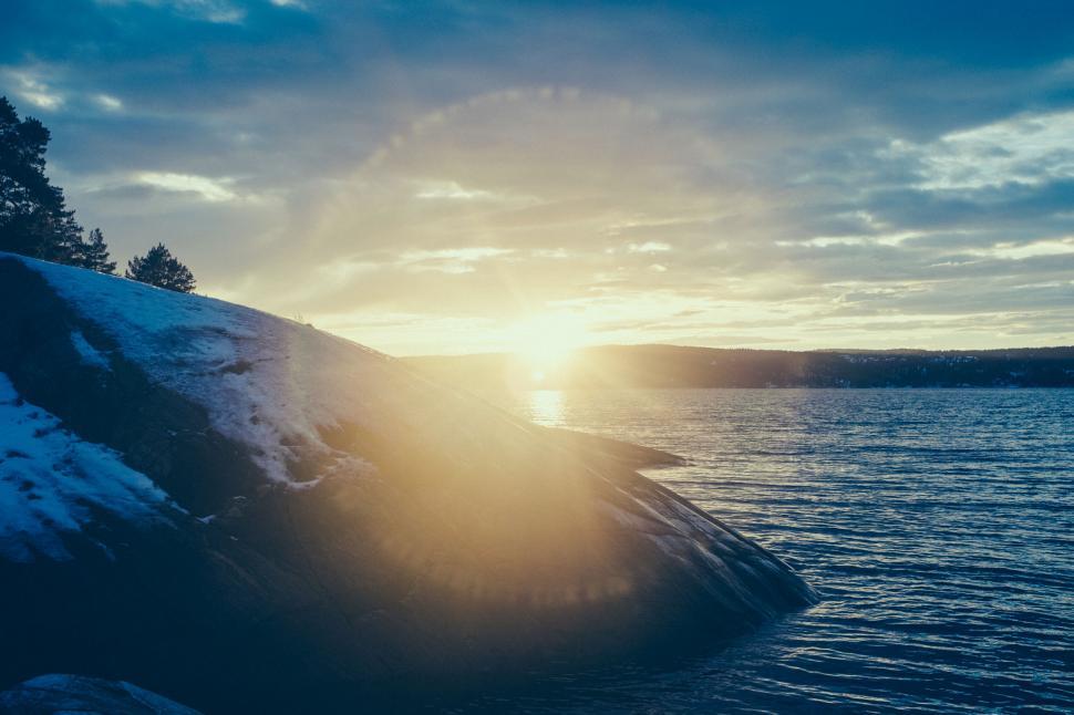 Free Image of Snowy lakeshore at dusk with radiant sun 