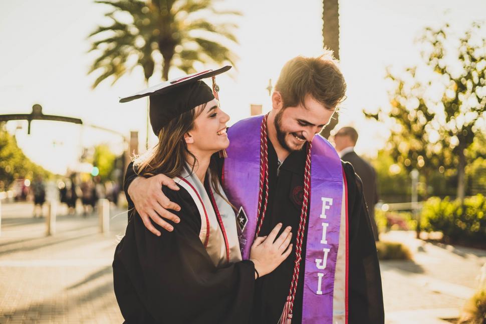 Free Image of Graduates embracing in caps and gowns during sunset 