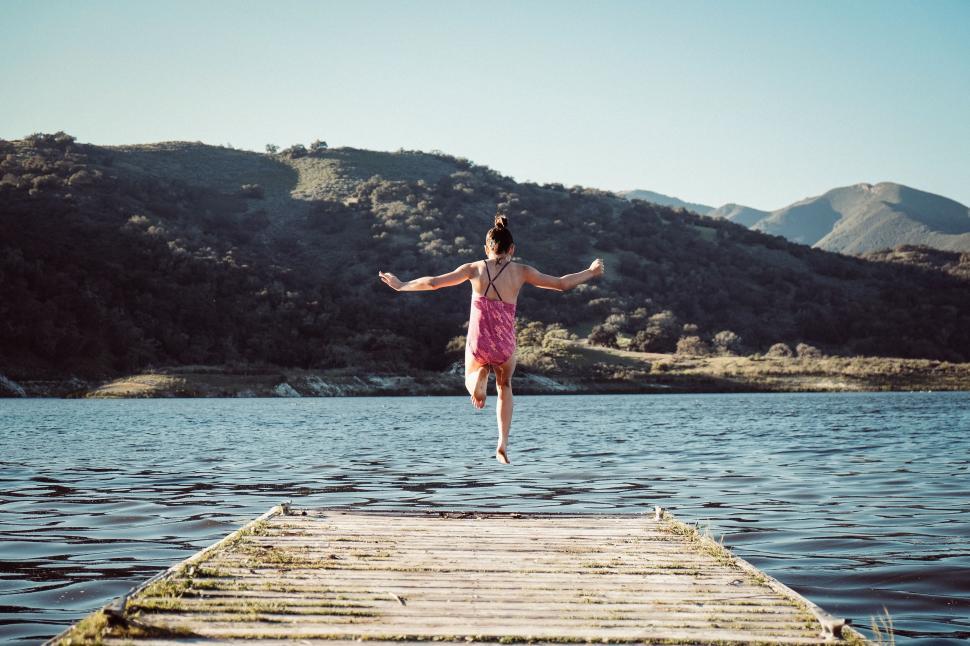 Free Image of Woman jumping off a wooden dock 