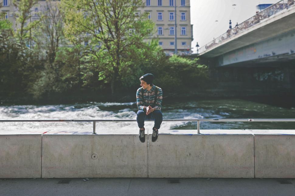 Free Image of Person sitting on ledge by the river 