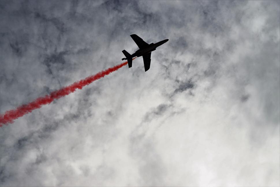 Free Image of Airplane flying high with red smoke trail 