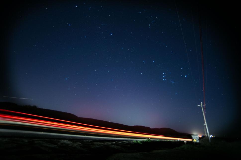 Free Image of Night sky with star trails over a road 
