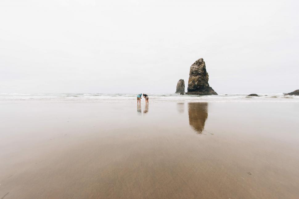 Free Image of Two people walking on a beach by a rock formation 
