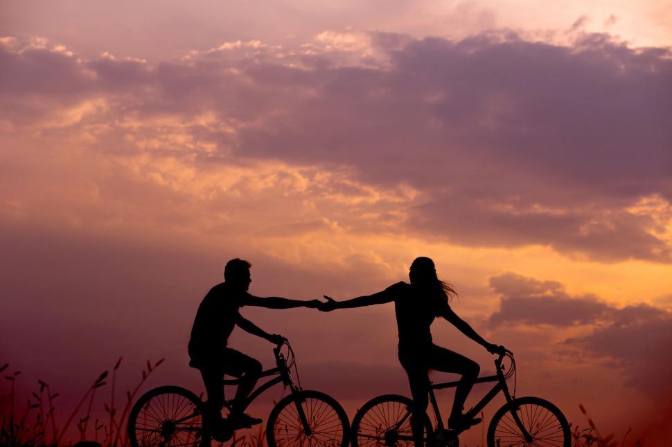 Free Image of Couple holding hands on bikes at dusk 