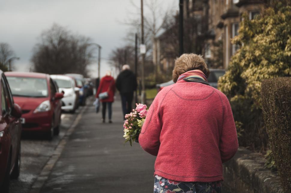 Free Image of Elderly person holding flowers walking on street 