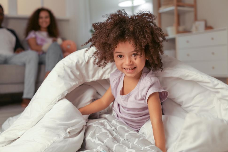 Free Image of Child playing in bed with parents in back 