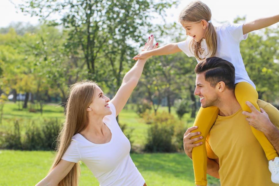Free Image of Family playing in sunny park with daughter on shoulders 