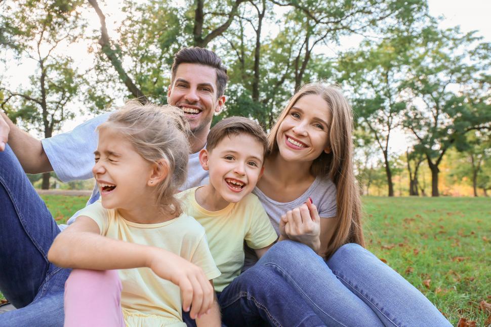 Free Image of Laughing family sitting on grass with trees 