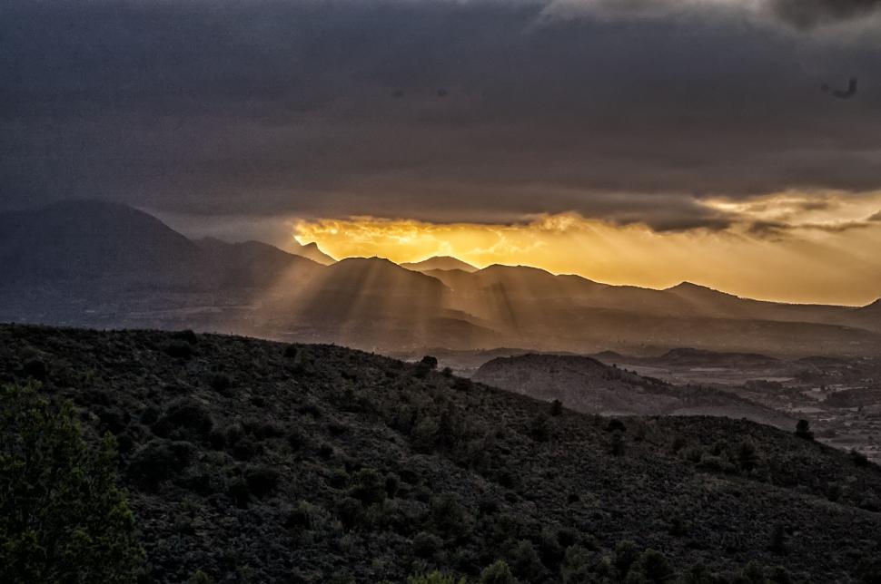 Free Image of Sun rays breaking through clouds over hills 