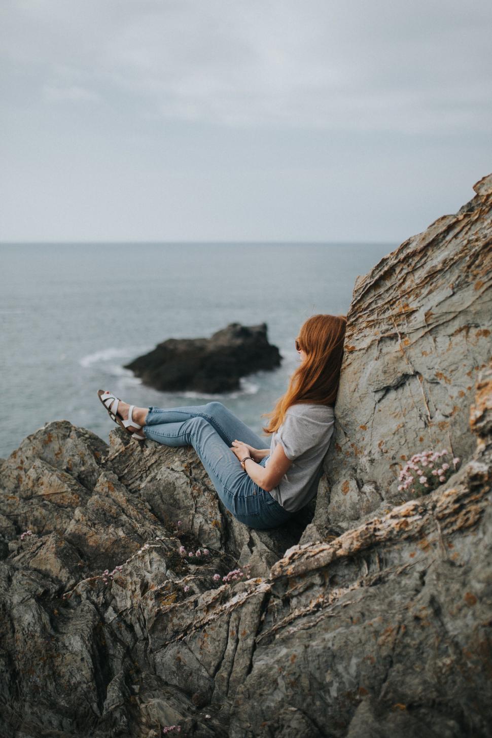 Free Image of Red-haired woman sitting on cliffside 