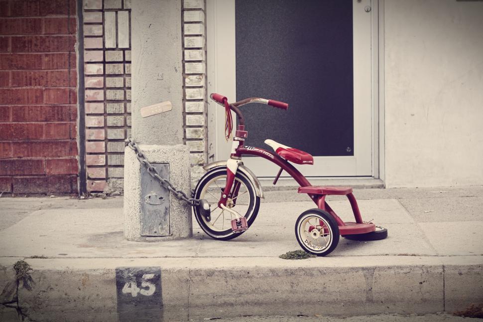 Free Image of Retro red tricycle parked on sidewalk 