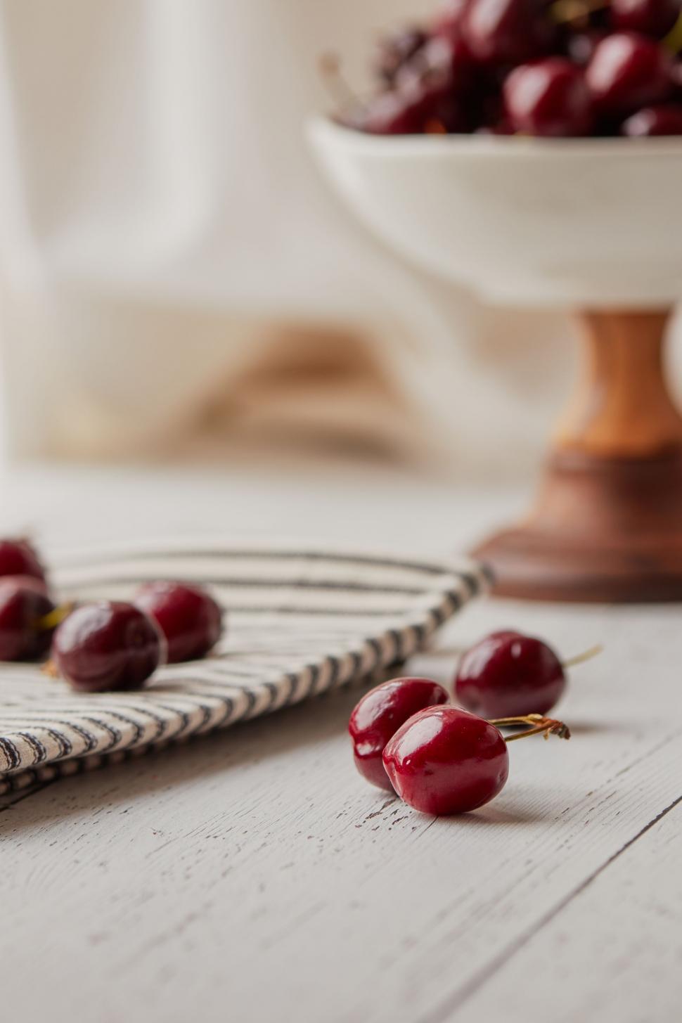 Free Image of Cherries scattered and bowl on white table 