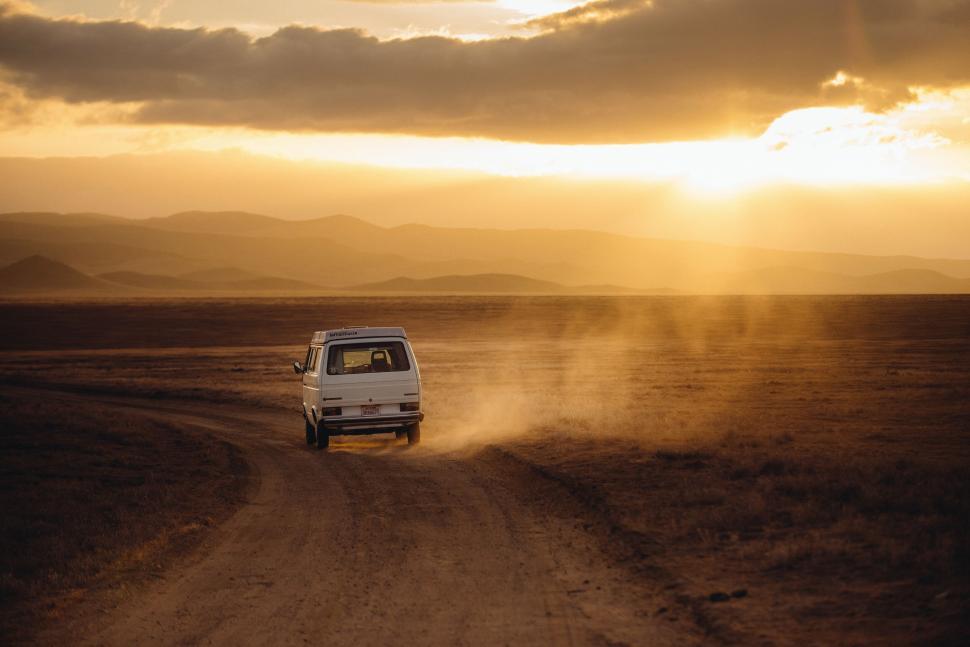 Free Image of Van driving on a dusty road at sunset 