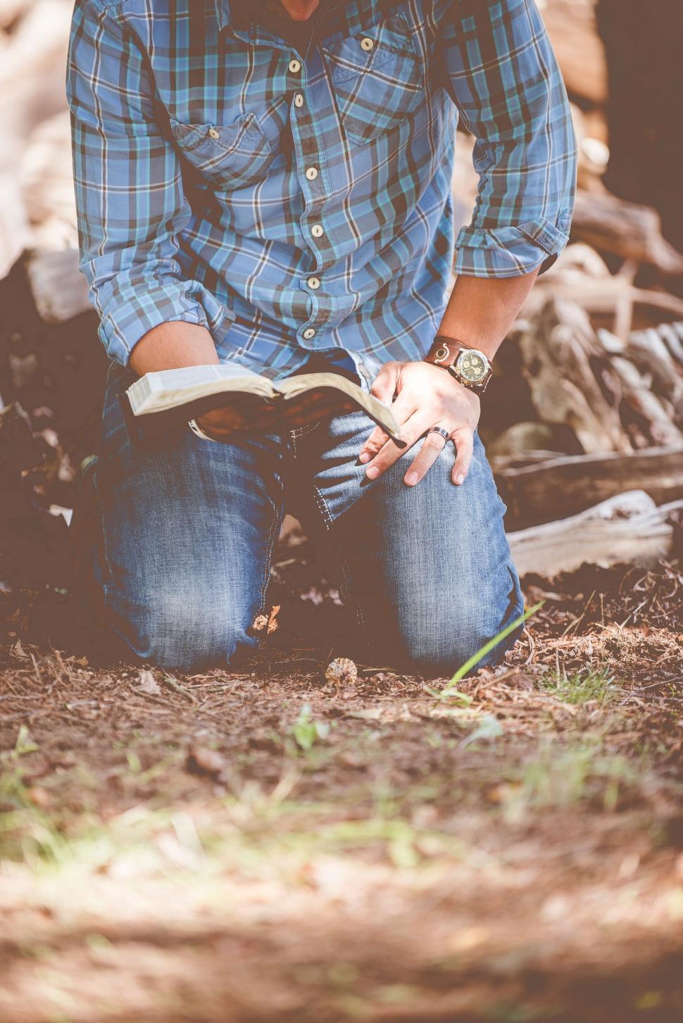 Free Image of Man kneeling and reading a book in nature 