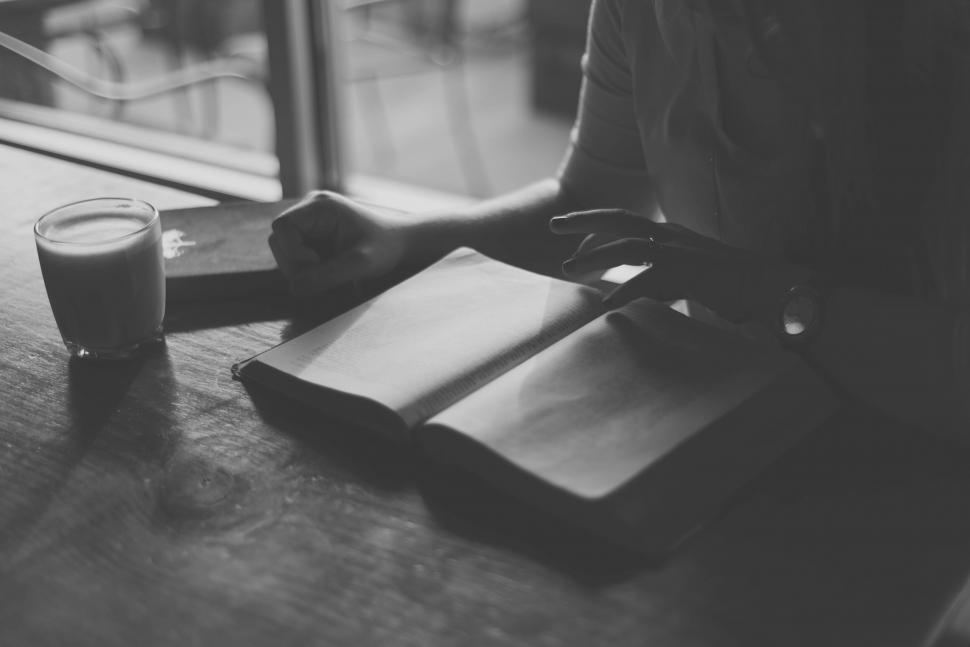 Free Image of Person holding a pen over a book in a cafe 