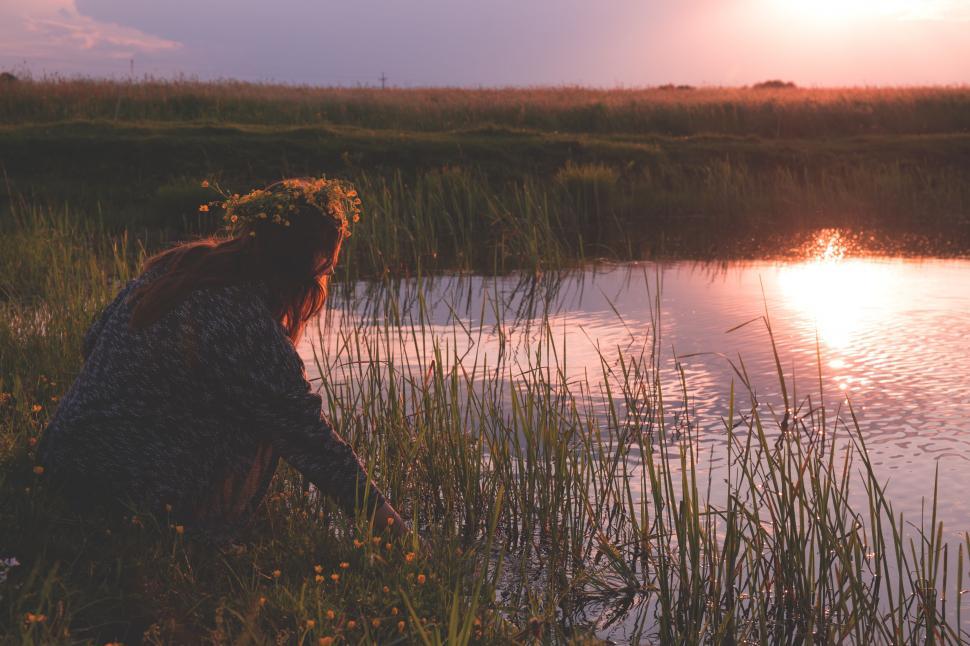 Free Image of Girl with a flower crown sitting by a pond at sunset 