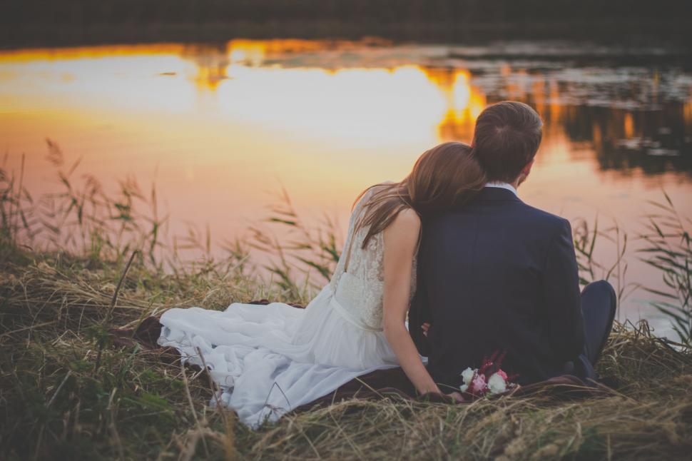Free Image of Wedding couple sitting by lakeside at sunset 