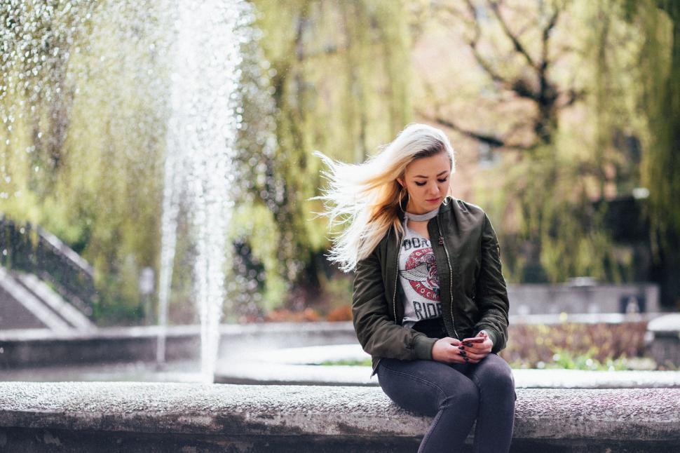 Free Image of Blonde woman texting by a fountain 