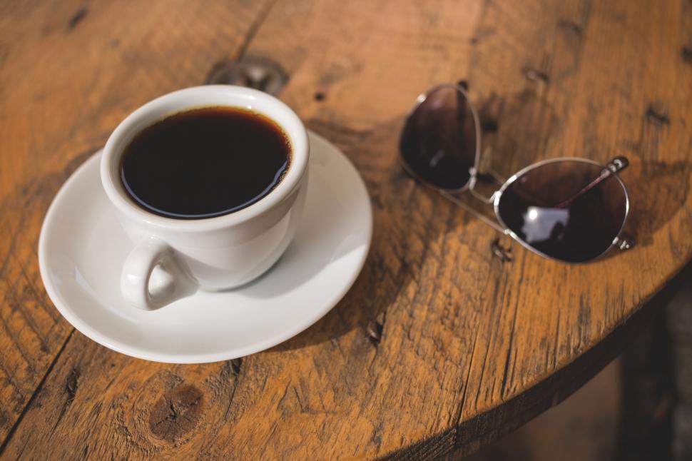 Free Image of Coffee cup on a wooden table with sunglasses 