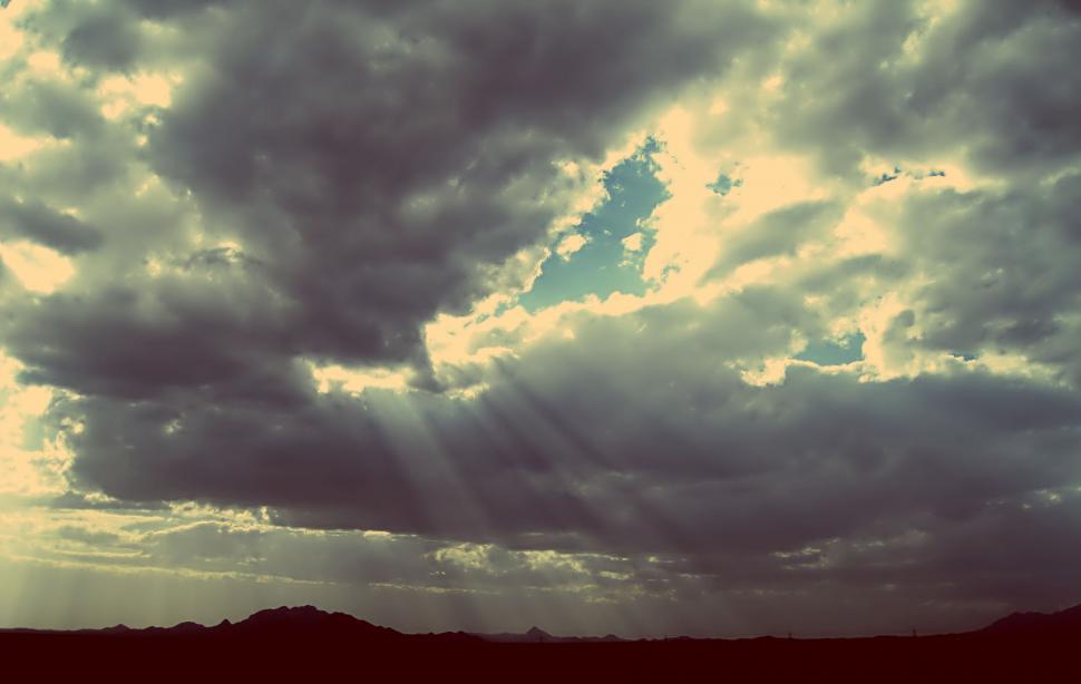 Free Image of Sunrays piercing through dramatic cloud cover 