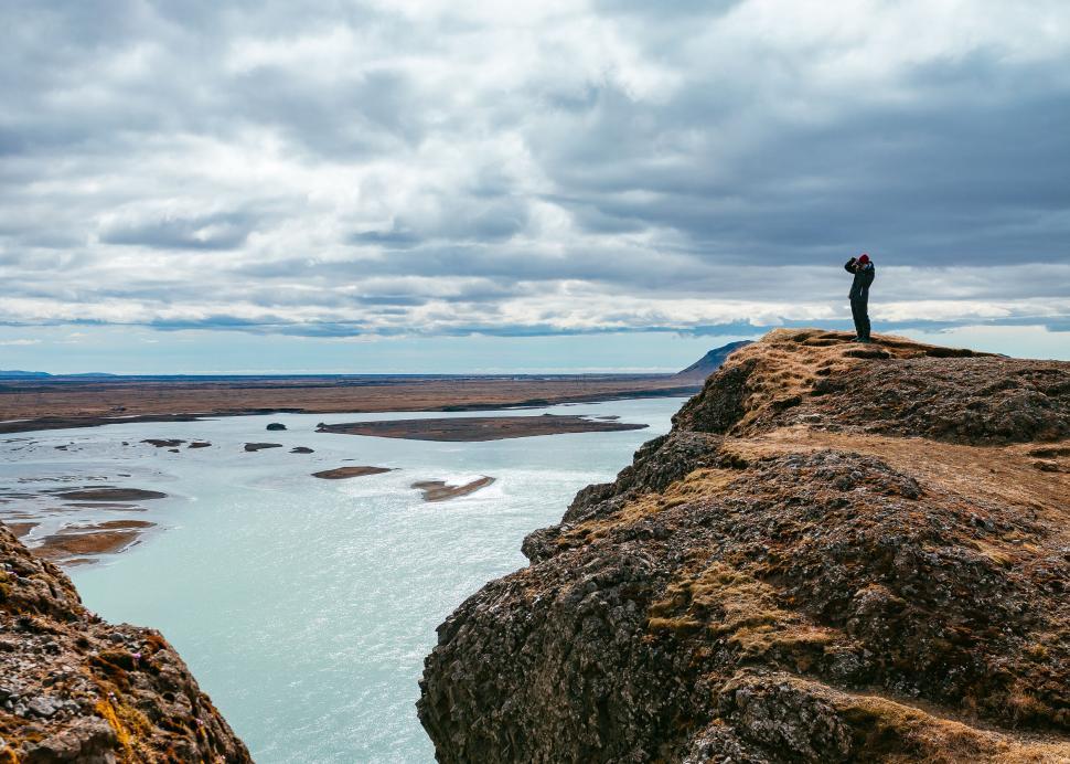 Free Image of Hiker on rocky outcrop overlooking water 