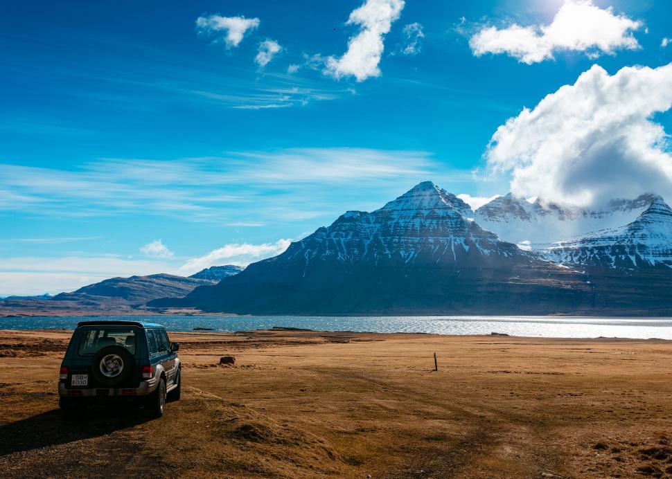 Free Image of SUV parked by a lake with mountains backdrop 