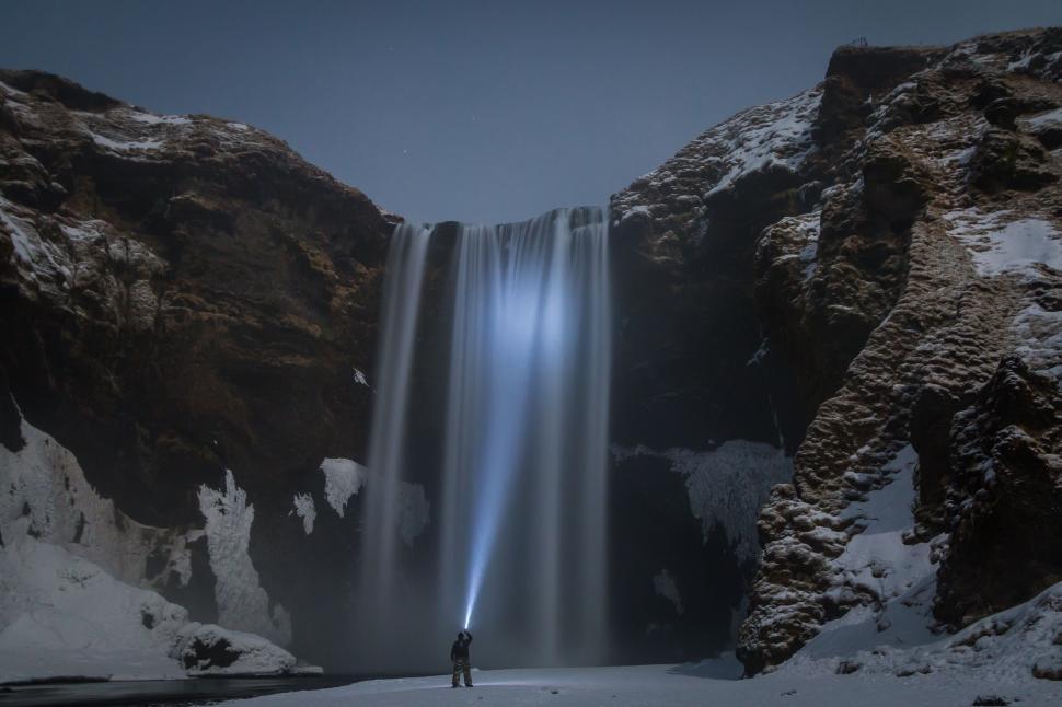 Free Image of Person illuminating majestic waterfall at night 