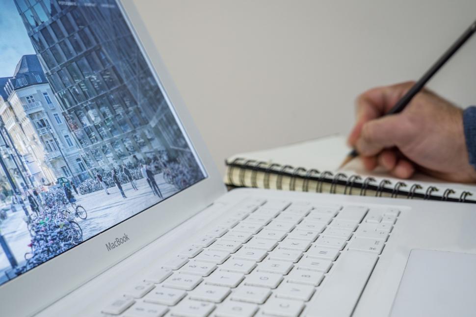 Free Image of Person writing in notebook by MacBook 