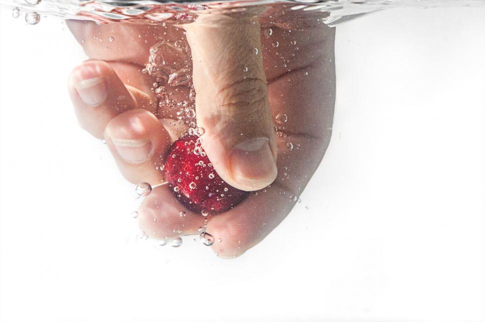 Free Image of Hand dipping strawberry into water with splashes 