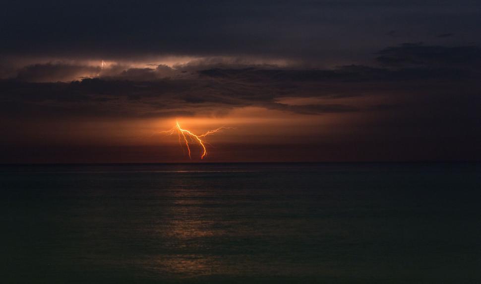 Free Image of Lightning strike over a calm sea at dusk 
