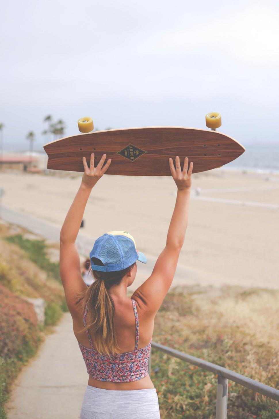 Free Image of Woman holding longboard over head at beach 