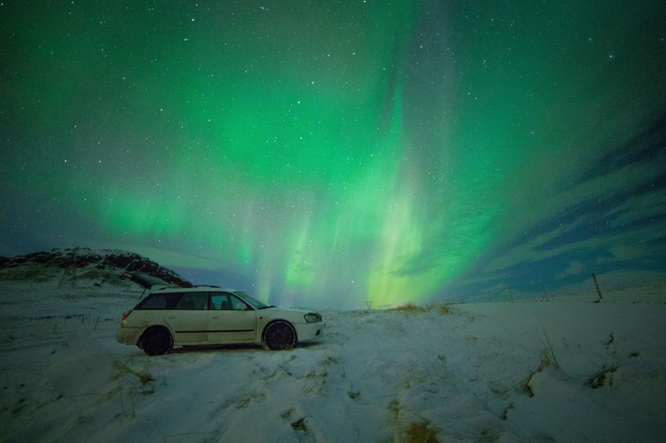 Free Image of Northern lights dazzling above a stranded car 