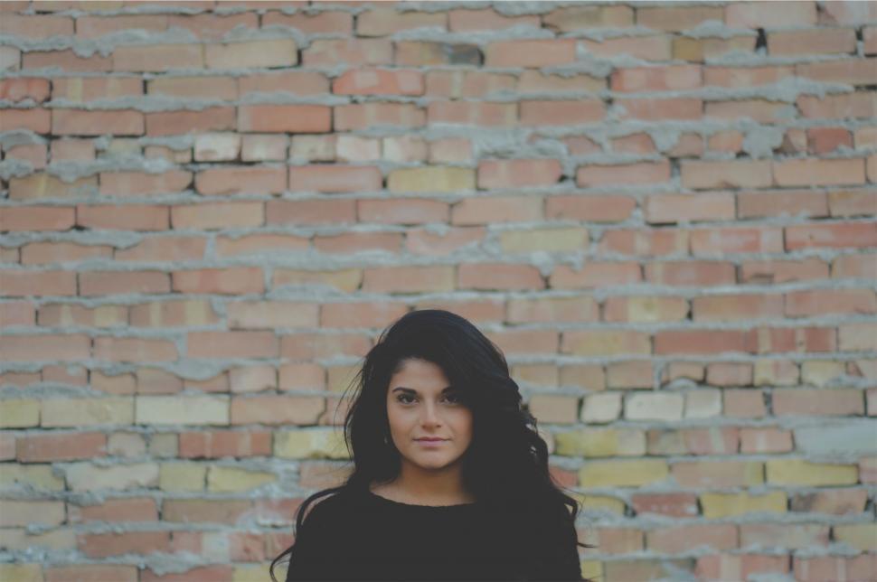 Free Image of Woman posing in front of brick wall 