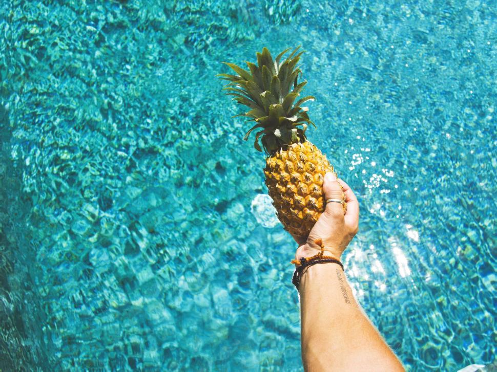 Free Image of Hand holding a pineapple over water 