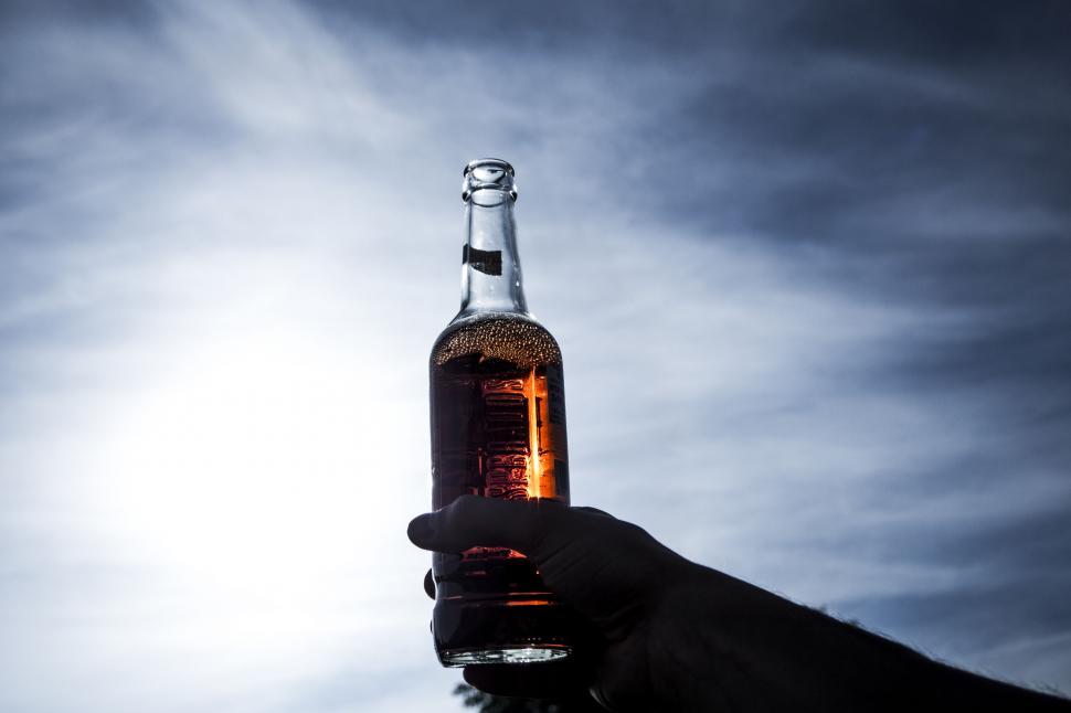 Free Image of Hand holding a beer bottle against cloudy sky 