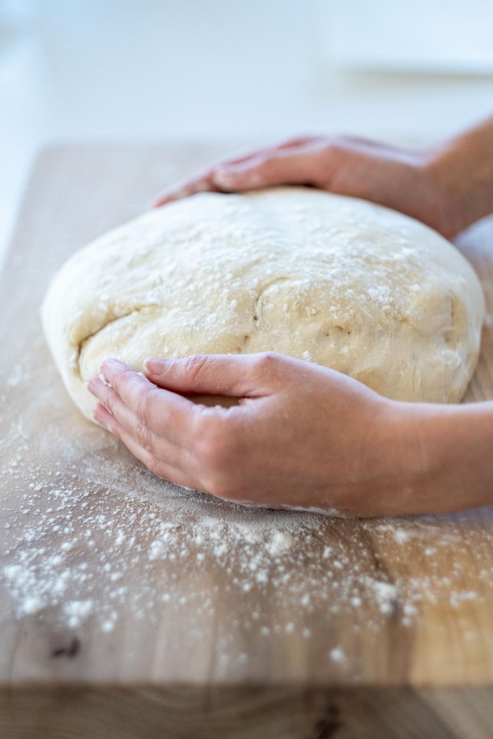 Free Image of Hands shaping a fresh loaf of bread on a cutting board 