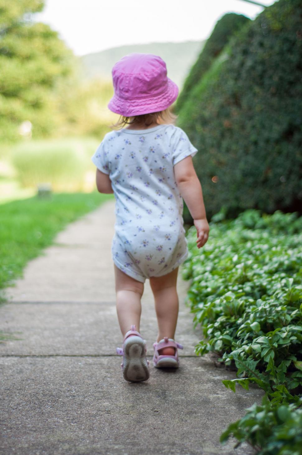 Free Image of Toddler walking on a paved path wearing a hat 